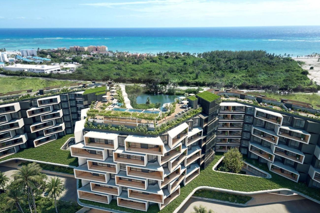 Recreación aérea de Makai Residences en Cap Cana: las dos alas con azoteas ajardinadas que albergan 216 residencias, con el lago, el arrecife y el mar al fondo.