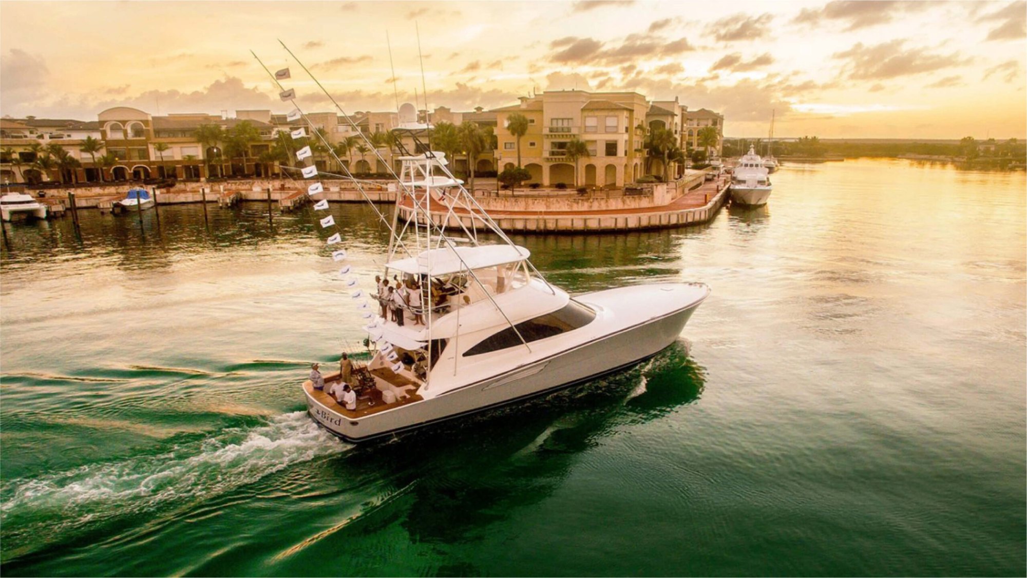 Photographie d'un bateau de pêche sportive quittant le chenal de la Marina Cap Cana au coucher du soleil, fanions de remise à l'eau au vent, à environ 4,4 miles de Makai par la route.